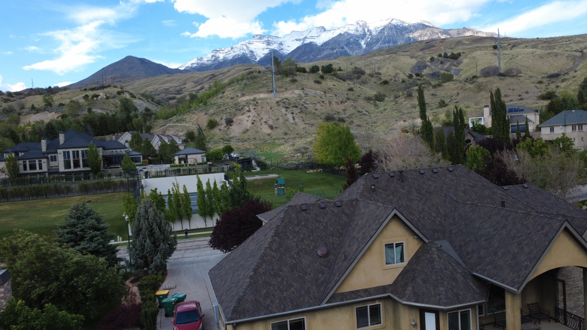Wide aerial of a Frame Restoration Utah completed reroof with snow-capped Mt. Timpanogos in the background — Wasatch Front, May 2026